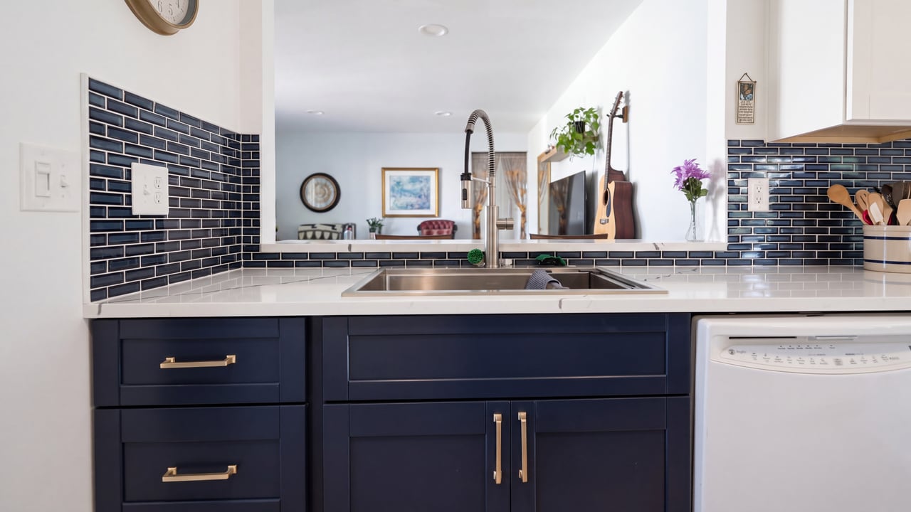 Kitchen sink and gold-toned faucet above navy blue cabinetry