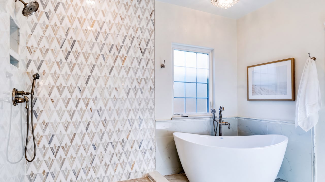 Patterned shower tile beside a freestanding bathtub and window