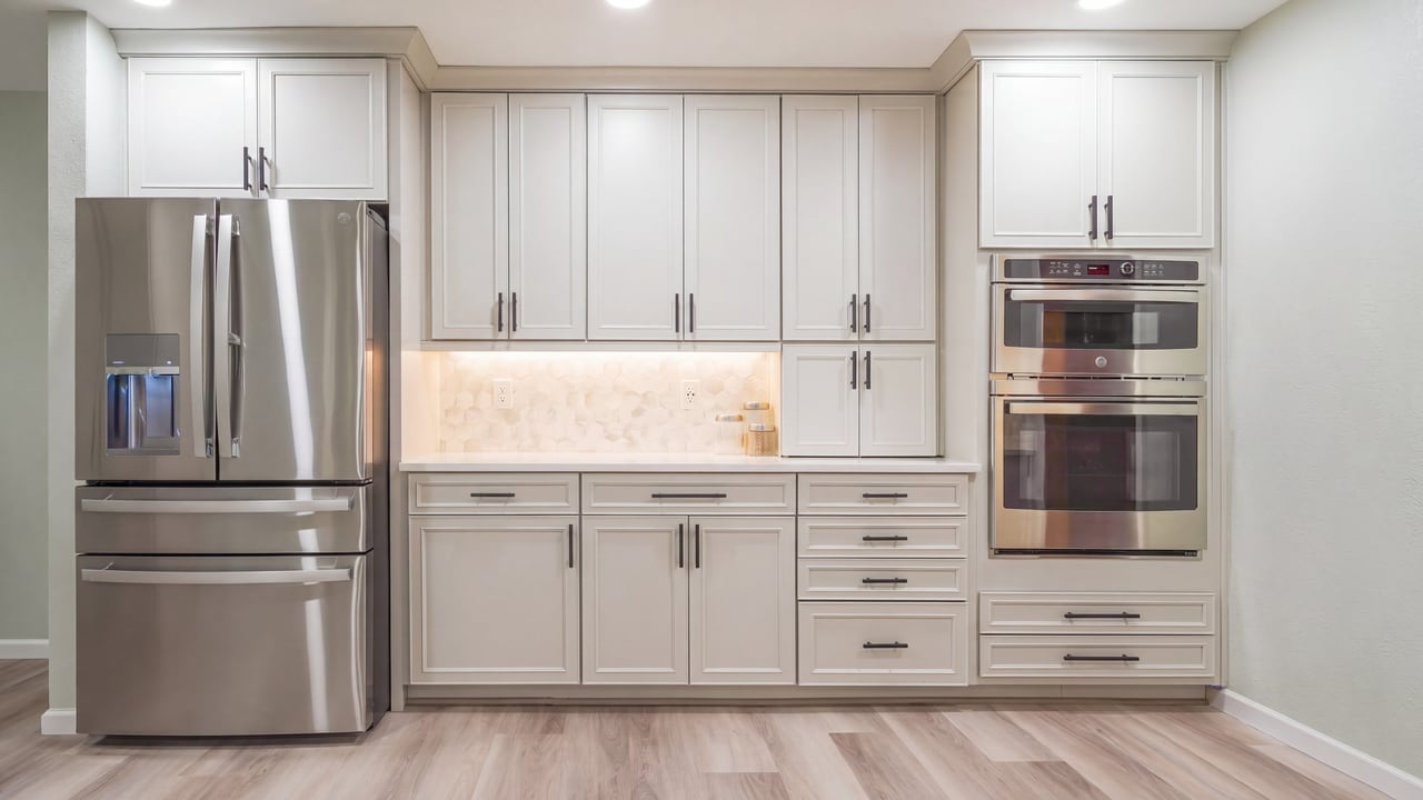 Stainless refrigerator and wall ovens fitted into white cabinetry
